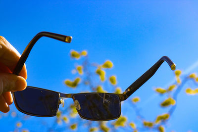 Close-up of hand holding sunglasses against clear blue sky