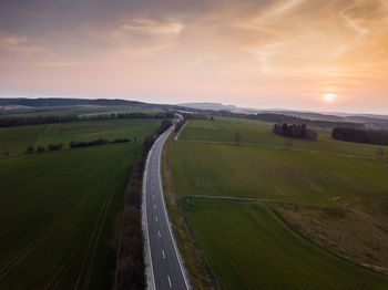 Road amidst agricultural field against sky during sunset