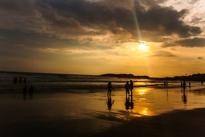 Silhouette people standing on beach against sky during sunset