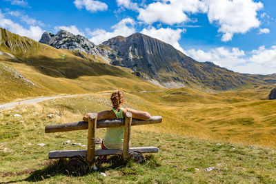 Rear view of woman sitting on bench in front of mountains