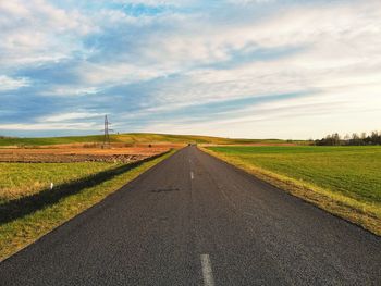 Empty road amidst field against sky