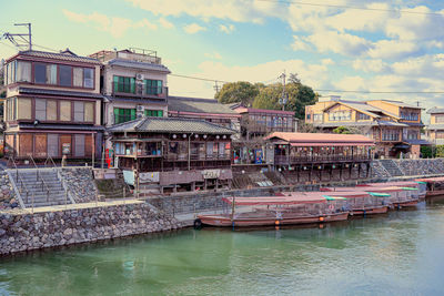 Boats moored in river by buildings against sky