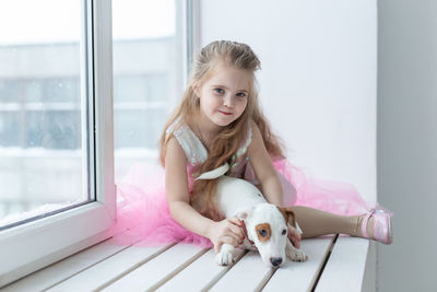 Portrait of cute girl with dog on window