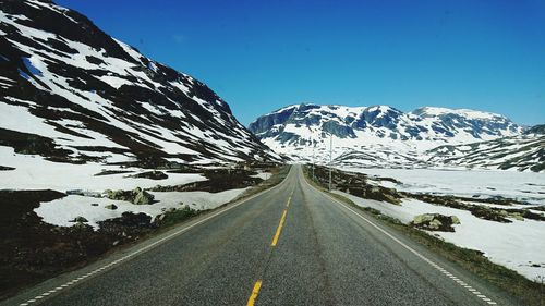 Road amidst snowcapped mountains against clear sky during winter