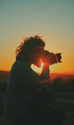 Man photographing with camera against sky during sunset