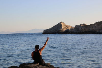 Rear view of woman sitting on rock by sea against sky