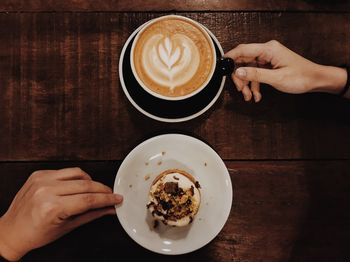 Close-up of hand holding cappuccino served on table