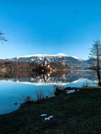 Scenic view of lake by snowcapped mountains against clear blue sky