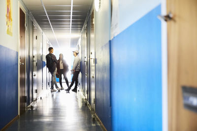 Full length of students talking while standing in corridor at university