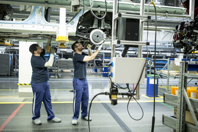 Two colleagues working at car underbody in modern factory