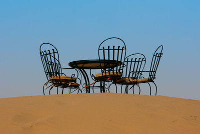 Chairs with bench on sand against clear sky