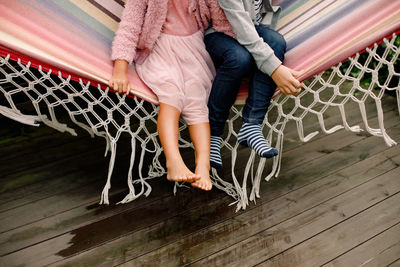 Low section of siblings sitting in hammock at backyard