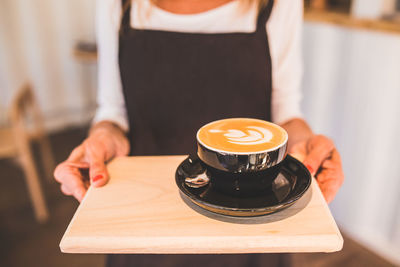 Midsection of woman holding coffee on table