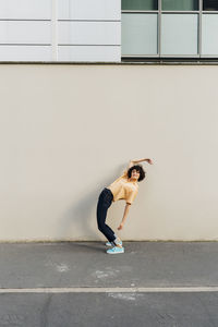 Woman with hand raised bending over backwards in front of wall
