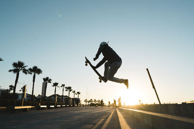 Side view of man performing stunt while skateboarding on road against sky