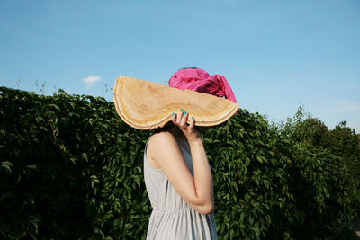 Midsection of woman holding hat against plants