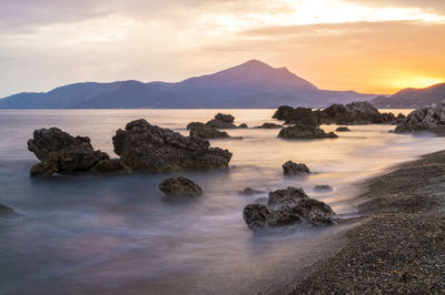 Rocks in sea against sky during sunset