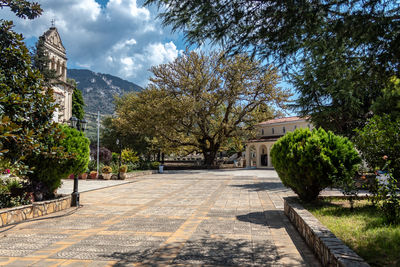 Footpath amidst trees and buildings against sky