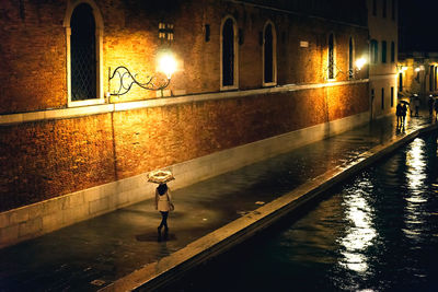 Wet illuminated street by canal at night