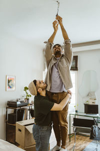 Side view of man embracing boyfriend installing bulb at home