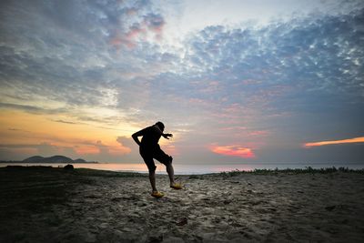 Rear view of man walking on sand against sky during sunset