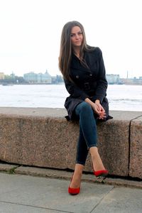 Young woman sitting on retaining wall against sea