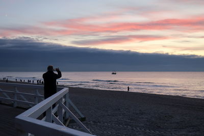 Rear view of man photographing at beach during sunset