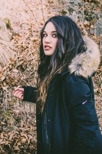 Side view portrait of young woman wearing fur coat against plants