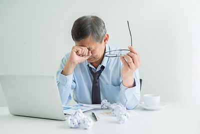 Tired businessman with crumpled papers and laptop sitting at desk in office