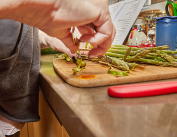 Chef prepares asparagus in the kitchen on wooden board according to recipe from the internet