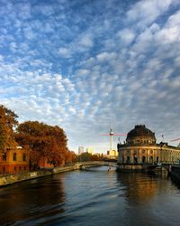 Canal by fernsehturm tower in city against cloudy sky