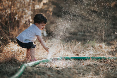 Baby girl standing by water spraying from hose on land