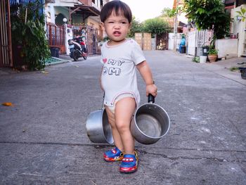 Cute toddler boy with cooking pans standing on street