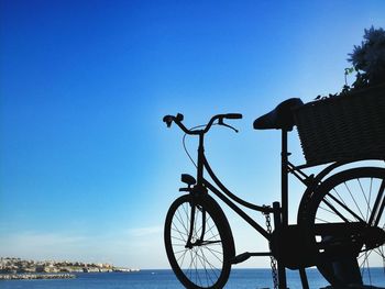 Low angle view of silhouette bicycle by sea against clear blue sky