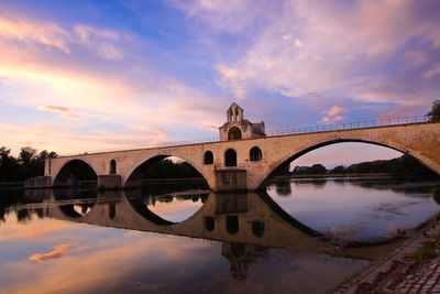 Arch bridge over river against sky during sunset