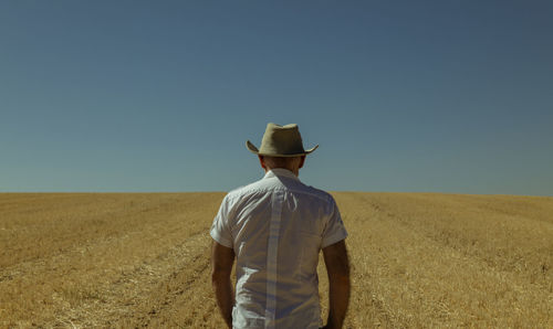 Rear view of man standing on field against clear sky