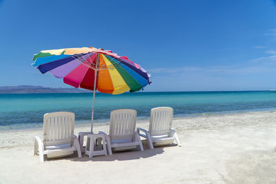 Deck chairs and parasol at beach against blue sky