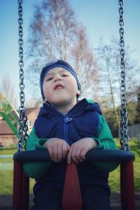 My cute boy is making funny faces while sitting on the swing