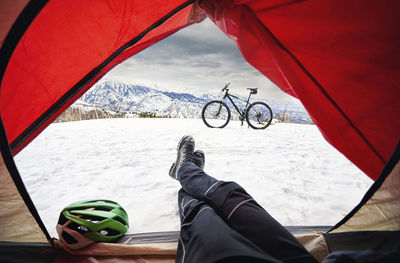 Low section of man relaxing in tent on snow covered mountain against sky