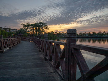 Footpath by railing against sky during sunset