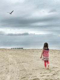 Rear view of girl walking on sand at beach against sky