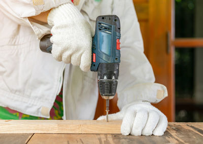 The carpenter ware white gloves screwing wooden bar with cordless screwdriver.