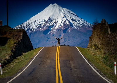 Man standing on road against snowcapped mountains