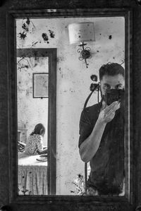 Reflection of man photographing with camera on mirror at home