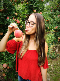 Close-up of smiling woman holding apple standing at farm