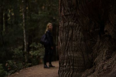 Woman standing by tree trunk in forest