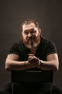 Portrait of man sitting against black background