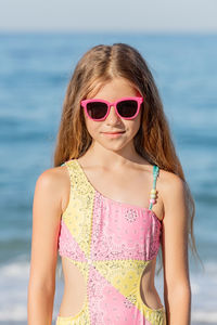 Girl posing on the beach in a pink swimsuit and glasses. vertical shot.
