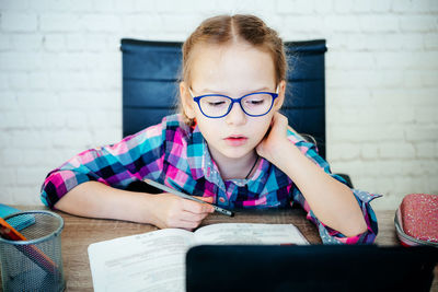 Little girl in eyeglasses studying online at home, a primary school girl with computer having zoom