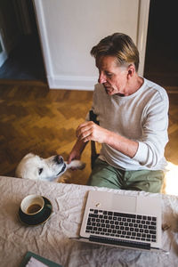 High angle view of senior man playing with dog while working on laptop from home